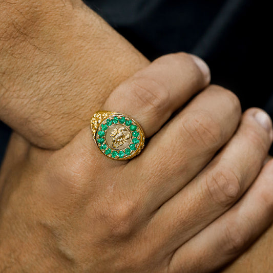 Mano de hombre usando anillo con forma de escorpión en el centro en oro amarillo de 18 quilates y piedras esmeraldas alrededor de color verde, hecho en Joyería Caracas.
