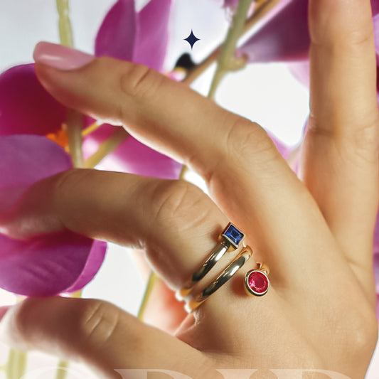 Mano de mujer con anillo en forma de espiral en oro amarillo de 18 quilates con cristal circular de color rojo y cristal cuadrado de color azul, hecho en Joyería Caracas.