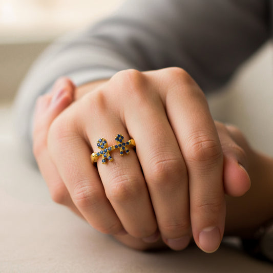 Mano de mujer usando un anillo en oro amarillo de 18 quilates con 2 formas de niños en el centro con cristales de color azul de Joyería Caracas.