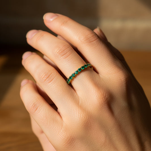 Mano de mujer usando un anillo sin fin en oro amarillo de 18 quilates con cristales de color verde alrededor de Joyería Caracas.