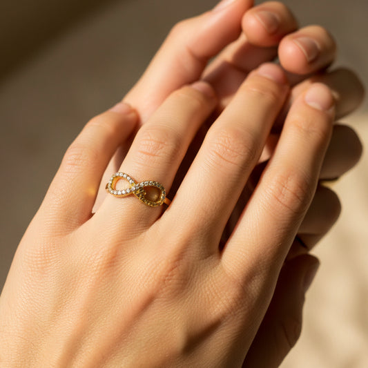 Mano de mujer usando un anillo con forma de infinito y la palabra promise en oro amarillo de 18 quilates con cristales de color blanco de Joyería Caracas.