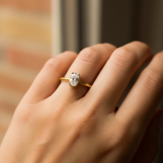 Mano de mujer usando un anillo en oro amarillo de 18 quilates con cristal ovalado de color blanco de Joyería Caracas.