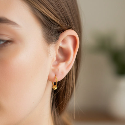 Oreja de modelo usando unos aretes sin fin con esfera en oro amarillo de 18 quilates de Joyería Caracas.