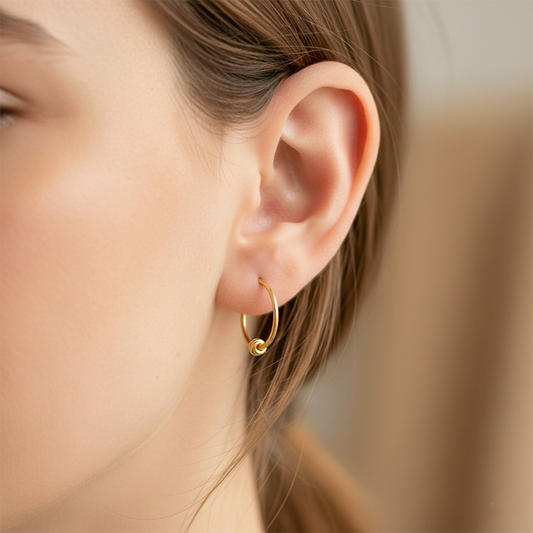 Oreja de modelo usando unos aretes sin fin con esfera en oro amarillo de 18 quilates de Joyería Caracas.