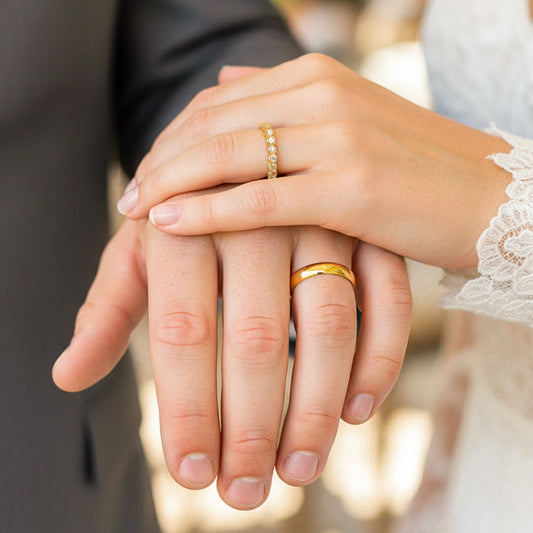 Mano de pareja en matrimonio usando unas argollas en oro amarillo de 18 quilates con cristales para dama y lisa para caballero de Joyería Caracas.