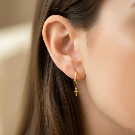 Oreja de modelo usando unas candongas lisas sin fin con dije en forma de cruz en oro amarillo de 18 quilates de Joyería Caracas.