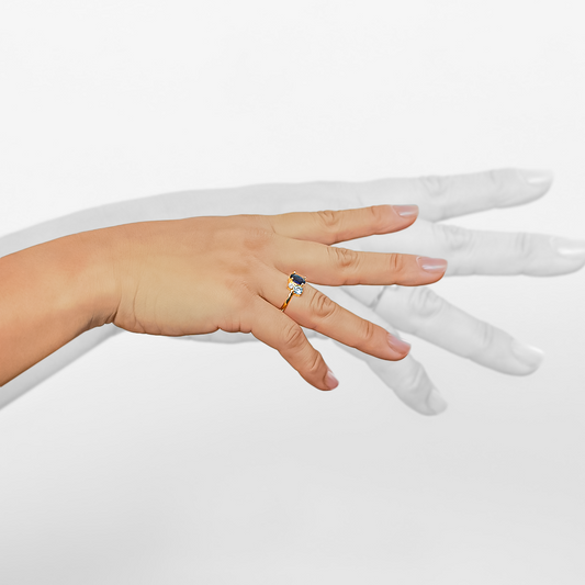 Mano de mujer usando un anillo en oro amarillo de 18 quilates con un piedra natural Amatista en forma de óvalo, un Diamante de color blanco redondo y un Topacio de color azul celeste redondo de Joyería Caracas.