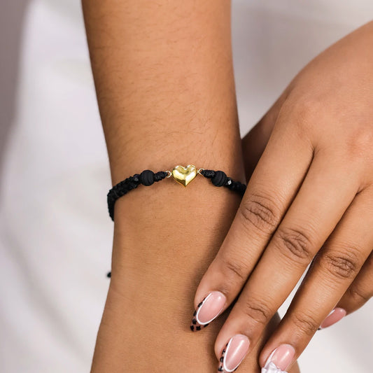 Mano de mujer con pulsera tejida en hilo negro terlenca, accesorios de bisutería en color negro y dije en forma de corazón en oro amarillo de 18 quilates, hecho en Joyería Caracas.