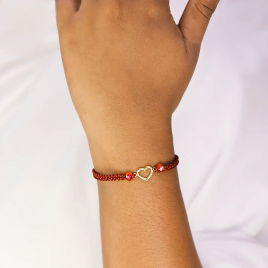 Mano de mujer con pulsera tejida en hilo rojo coreano, accesorios de bisutería en color rojo y dije con forma de corazón de silueta, hecho en Joyería Caracas.