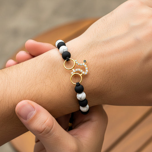 Mano de modelo usando una pulsera tejida en hilo color negro con dije en forma de bicicleta en oro amarillo de 18 quilates con cristales de color blanco y bisutería de calidad de Joyería Caracas.