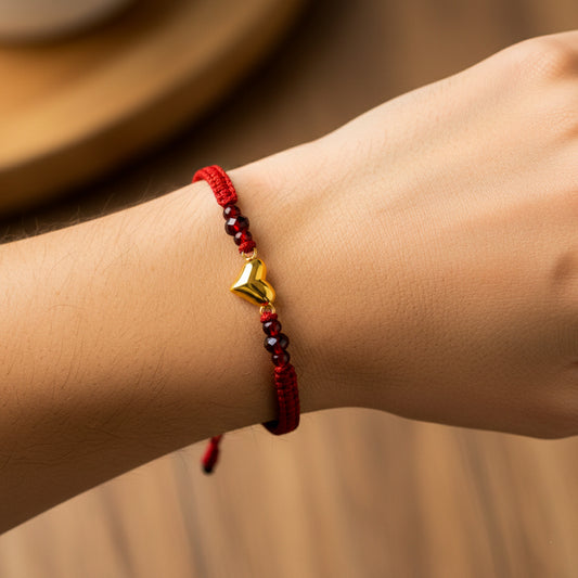 Mano de modelo usando una pulsera tejida en hilo color rojo con dije en forma de corazón en oro amarillo de 18 quilates con bisutería de calidad de Joyería Caracas.
