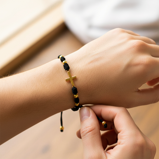 Mano de modelo usando una pulsera tejida en hilo color negro, con cruz y esferas facetadas en oro amarillo de 18 quilates de Joyería Caracas.
