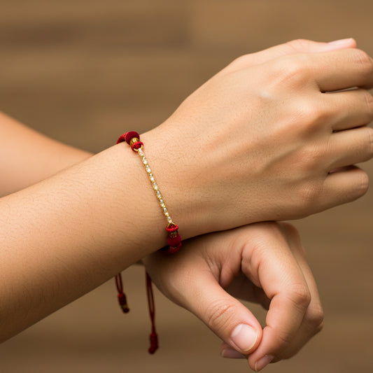 Mano de modelo usando una pulsera tejida en hilo de color rojo con tejido escalera 3 oros de 18 quilates con bisutería de calidad de Joyería Caracas.
