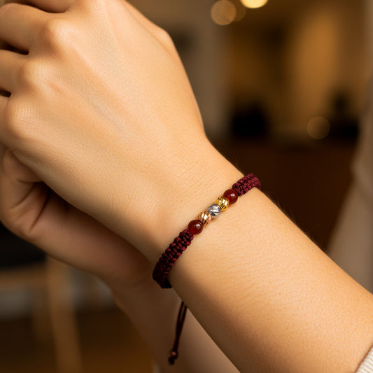 Mano de modelo usando una pulsera tejida en hilo color vinotinto, con 3 esferas facetadas en 3 oros de 18 quilates con bisutería de calidad de Joyería Caracas.