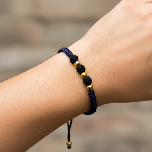 Mano de modelo usando una pulsera tejida en hilo color azul oscuro con 3 esferas lisas en oro amarillo de 18 quilates y bisutería de calidad de Joyería Caracas.