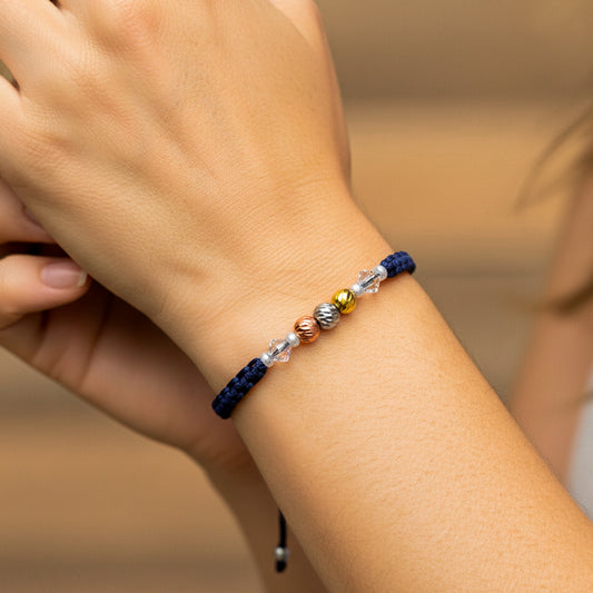 Mano de modelo usando una pulsera tejida con hilo de color azul, 3 esferas facetadas tres oros y bisutería de calidad.