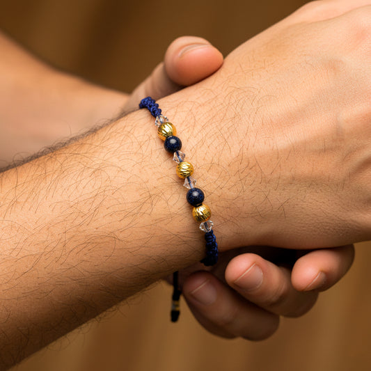 Mano de modelo usando una pulsera tejida en hilo color azul oscuro, 3 esferas facetadas en oro amarillo de 18 quilates con bisutería de calidad de Joyería Caracas.