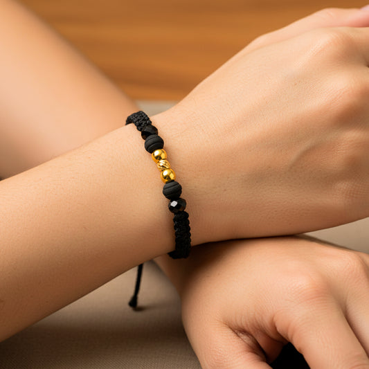 Mano de modelo usando una pulsera tejida con hilo color negro, con esferas lisas y facetada en oro amarillo de 18 quilates con bisutería de calidad de Joyería Caracas.
