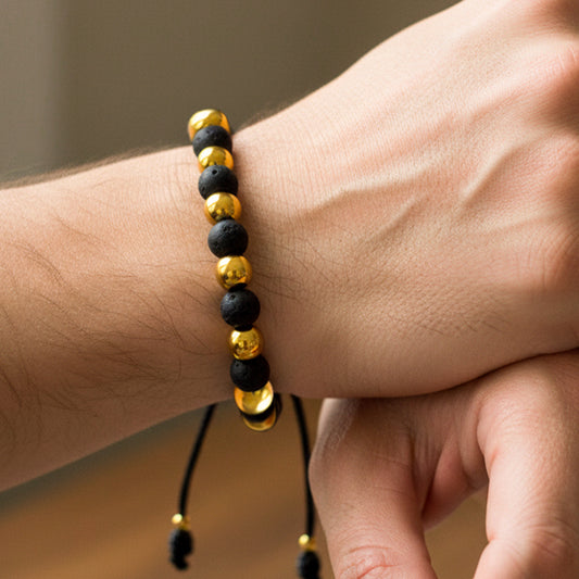 Mano de modelo usando una pulsera tejida en hilo de color negro con esferas lisas en oro amarillo de 18 quilates con bisutería de calidad.