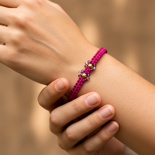 Mano de modelo usando una pulsera tejida en hilo color fucsia con 2 esferas lisas en oro amarillo de 18 quilates con bisutería de calidad de Joyería Caracas.