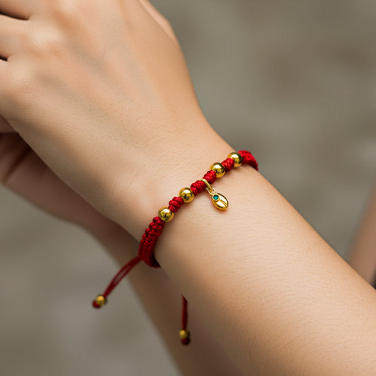 Mano de modelo usando una pulsera tejida de hilo color rojo con dije en forma de grano de café con esferas lisas en oro amarillo de 18 quilates de Joyería Caracas.