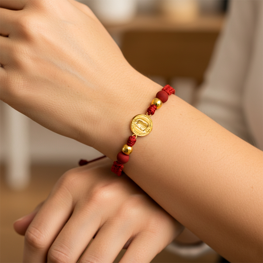 Mano de modelo usando una pulsera tejida en hilo color rojo con dije de la Virgen de Guadalupe y esferas lisas en oro amarillo de 18 quilates de Joyería Caracas.