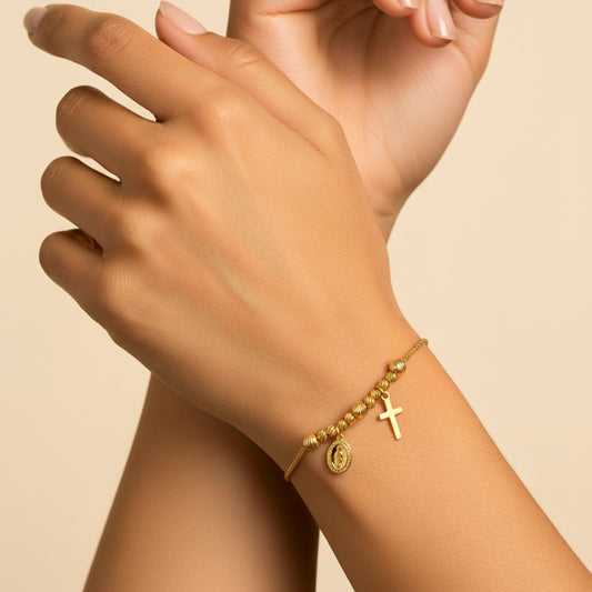 Mano de mujer usando una pulsera con esferas facetadas, dije de la virgen de Guadalupe y cruz en oro amarillo de 18 quilates de Joyería Caracas.