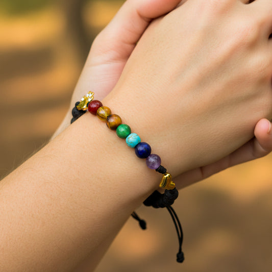 Mano de modelo usando una pulsera tejida en hilo color negro, con herraje en forma de corazón y puente de arcoíris en oro amarillo de 18 quilates con bisutería de calidad de Joyería Caracas.