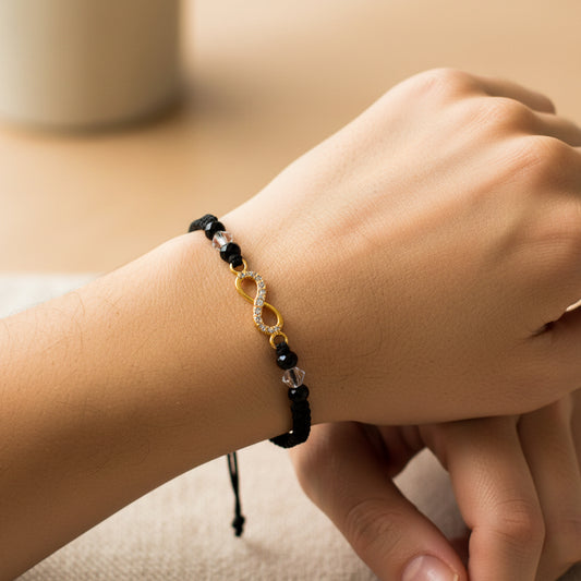 Mano de modelo usando una pulsera tejida en hilo color negro con dije de infinito en oro amarillo de 18 quilates con bisutería de calidad de Joyería Caracas.