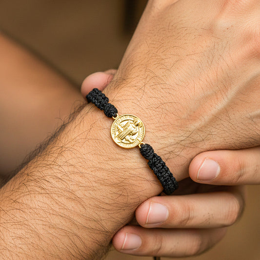 Mano de hombre usando una pulsera tejida con herraje de San Benito en oro amarillo de 18 quilates de Joyería Caracas.