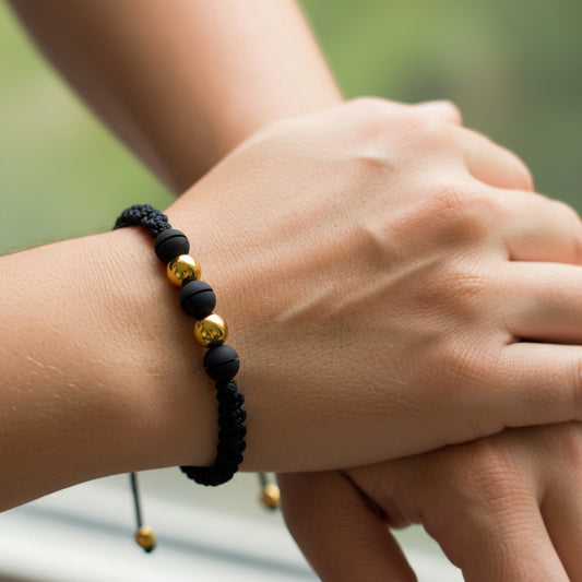 Mano de modelo usando una pulsera tejida en hilo color negro con 2 esferas lisas en oro amarillo de 18 quilates y bisutería de calidad de Joyería Caracas.