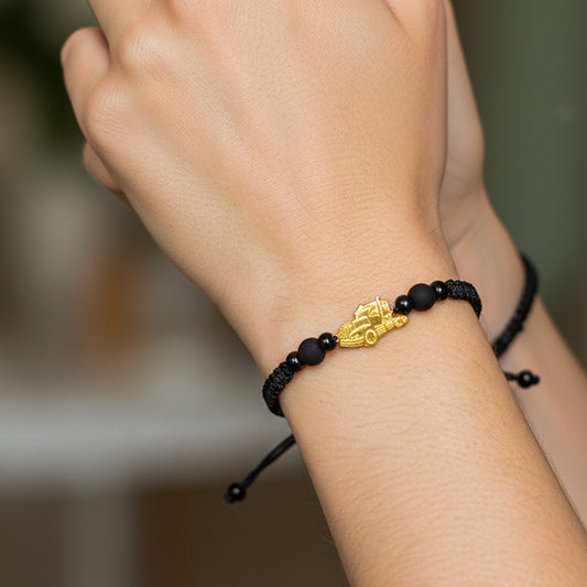 Mano de modelo usando unas pulsera tejida en hilo color negro con herraje de tracto mula en oro 18k de Joyería Caracas.