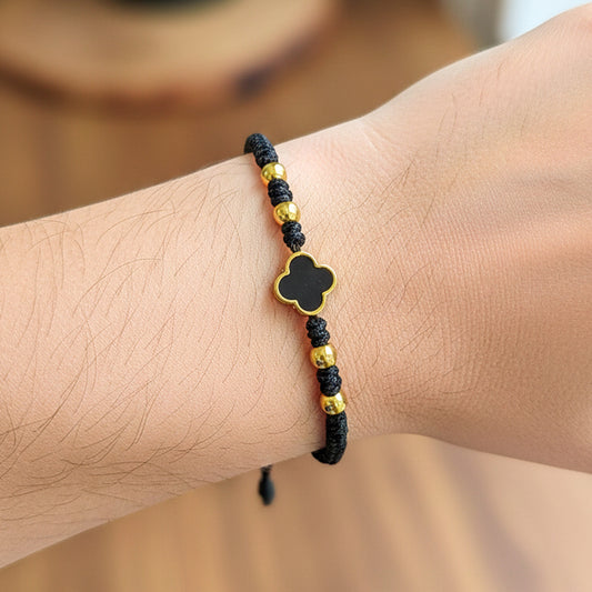 Mano de modelo usando una pulsera tejida en hilo color negro con herraje en forma de trébol y esferas lisas en oro 18 quilates de Joyería Caracas.