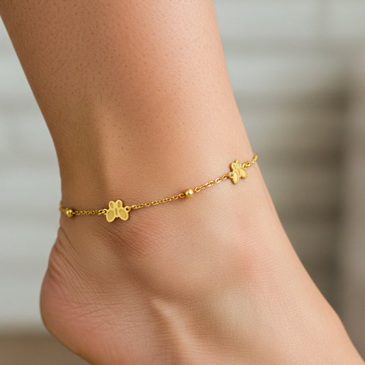 Tobillo de mujer usando una tobillera de mariposas y esferas lisas en oro amarillo de 18 quilates de Joyería Caracas.