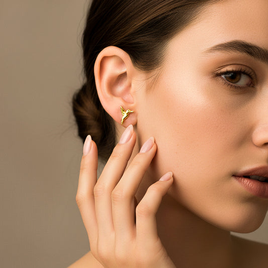 Oreja de modelo usando un topito en forma de colibrí en oro amarillo de 18 quilates de Joyería Caracas.