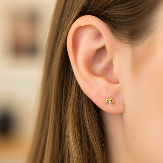 Oreja de modelo usando un topito en forma de delfín en oro amarillo de 18 quilates con cristal de Joyería Caracas.