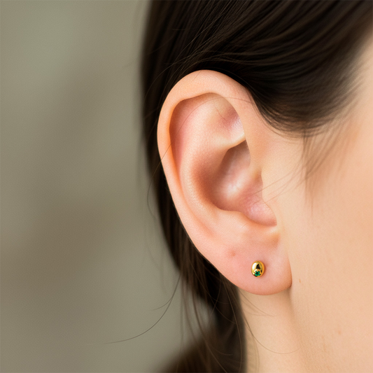 Oreja de modelo usando un topito en forma de grano de café en oro amarillo de 18 quilates con esmeralda de Joyería Caracas.