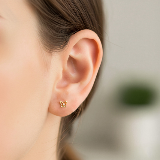 Oreja de modelo usando un topito en forma de mariposa en oro amarillo de 18 quilates con cristal de color blanco de Joyería Caracas.