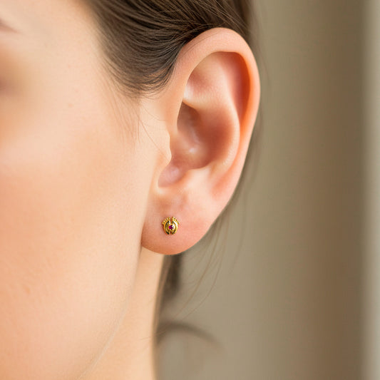 Oreja de modelo usando un topito en forma de pies descalzos en oro amarillo de 18 quilates con cristal en el centro de Joyería Caracas.