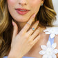 Mano de mujer con anillo inspirado en las palmeras de Miami, en oro blanco de 18 quilates con cristales de color blanco alrededor y celeste en el centro.
