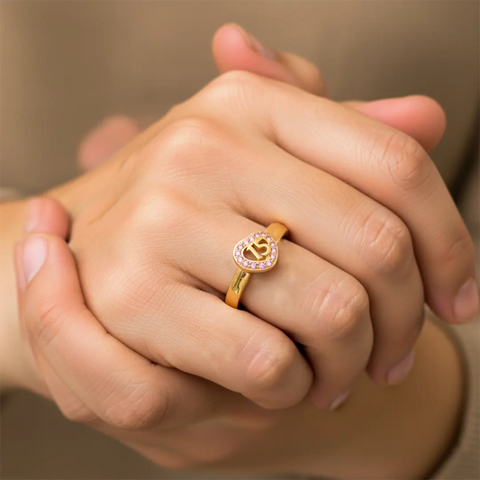 Mano de mujer usando un anillo con forma de corazón en el centro con el número 15 en el centro en oro amarillo de 18 quilates con cristales de color rosado de Joyería Caracas. 