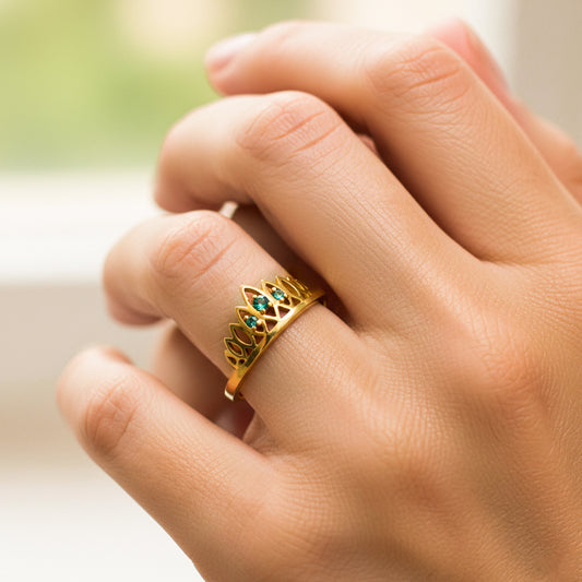 Mano de mujer usando un  anillo en forma de corona en oro amarillo de 18 quilates con 3 cristales de color verde de Joyería Caracas. 