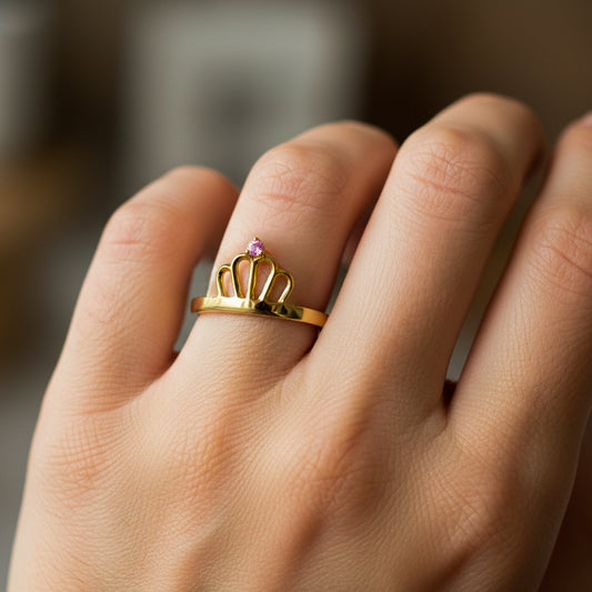 Mano de mujer usando un anillo con forma de corona en oro amarillo de 18 quilates con cristal redondo de color rosado de Joyería Caracas. 