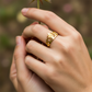 Mano de mujer usando un anillo con forma de corona en oro amarillo de 18 quilates con cristales rosados de Joyería Caracas. 