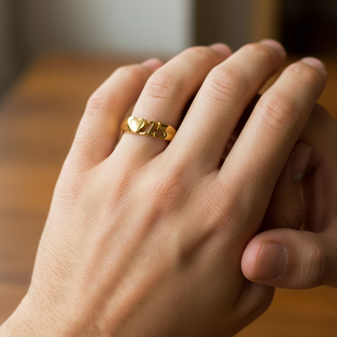 Mano de mujer usando un anillo con forma de corazón y el número 15 en el centro en oro amarillo de 18 quilates de Joyería Caracas.