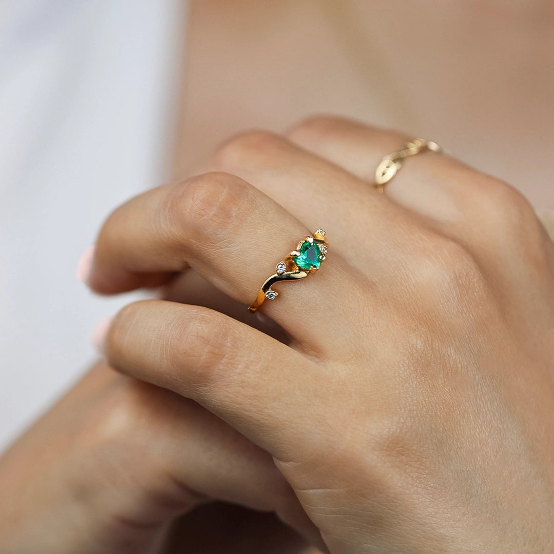 Mano de mujer usando un anillo en oro amarillo de 18 quilates en forma de onda el aro con hojas y Esmeralda en el centro en forma de corazón y cristales de color blanco en las hojas de Joyería Caracas.