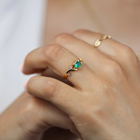 Mano de mujer usando un anillo en oro amarillo de 18 quilates en forma de onda el aro con hojas y Esmeralda en el centro en forma de corazón y cristales de color blanco en las hojas de Joyería Caracas.