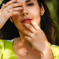 Mano de mujer usando un anillo en oro amarillo de 18 quilates con Diamante en el centro en forma redonda de color blanco y 2 Esmeraldas en forma de gota de color verde de Joyería Caracas. 