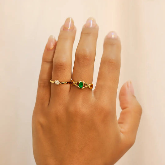 Mano de mujer usando anillo con forma de infinito en oro amarillo de 18 quilates y piedra preciosa Esmeralda en el centro en forma óvalo, fabricado en Joyería Caracas. 