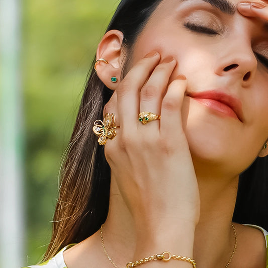 Mano de mujer con anillo en forma de mariposa en oro amarillo de 18 quilates con cristales de color verde y blanco, hecho en Joyería Caracas. 